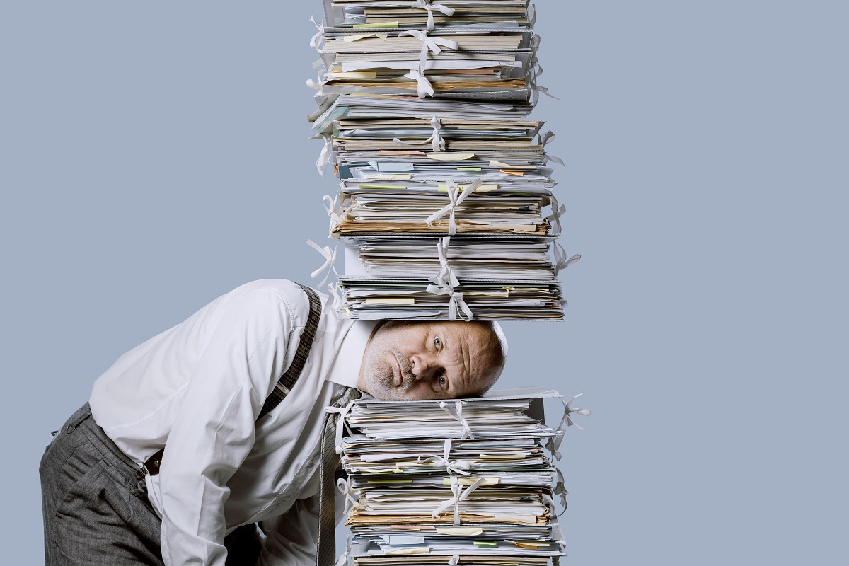 Comment choisir un prestataire de destruction d’archives Homme d'affaires stressé sous une pile de paperasse