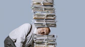 Comment choisir un prestataire de destruction d’archives Homme d'affaires stressé sous une pile de paperasse